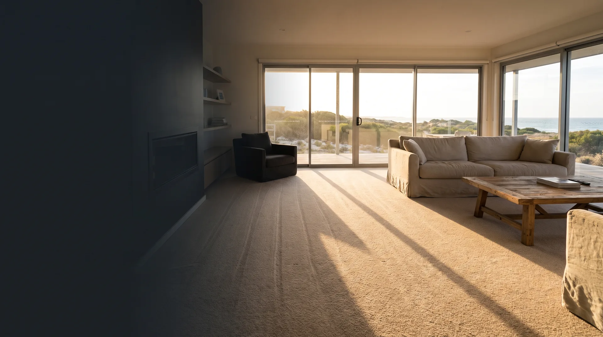 A beach house living room with late afternoon light across freshly cleaned carpet and the dunes through the glass