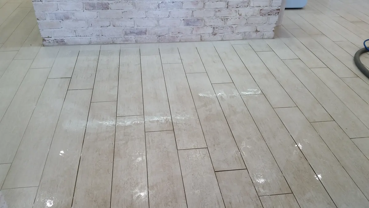 A plank-format tiled floor with pale marks and residue before cleaning