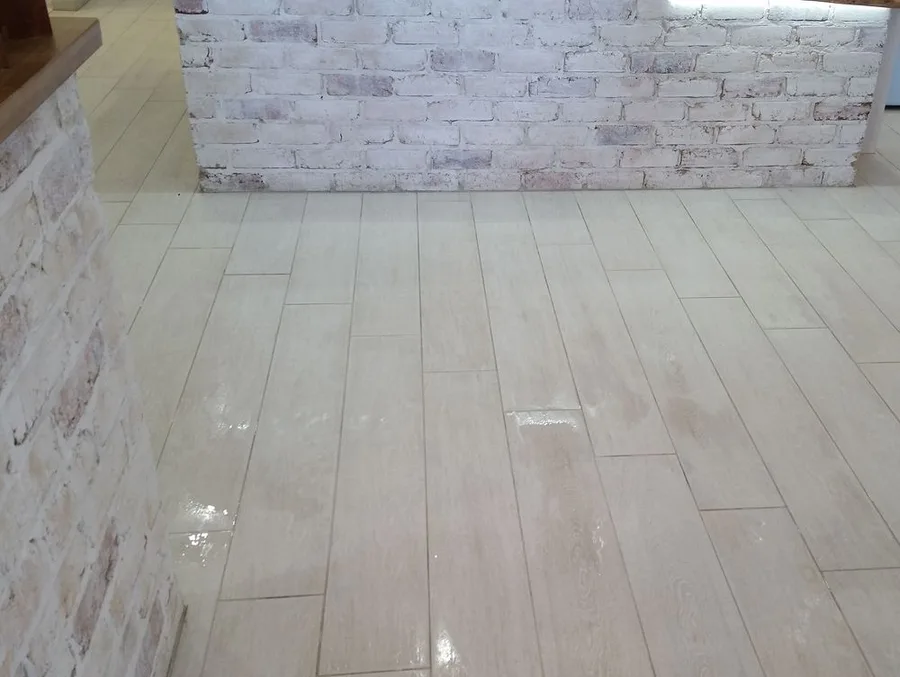 A plank-format tiled floor freshly cleaned and still wet, beside a whitewashed brick wall